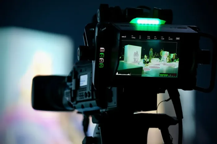 Professional video camera captures an event, green light illuminated.